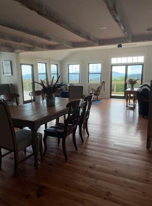 A spacious dining area with a wooden table and chairs, large windows offering a view of the outdoors, and a balcony with a view of the mountains. - Dog Friendly, Modern Retreat w/ Stunning View (Freedom)