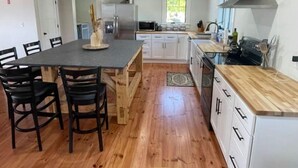 A modern kitchen with a central island, wooden chairs, white cabinets, and a large window. - Dog Friendly, Modern Retreat w/ Stunning View (Freedom)