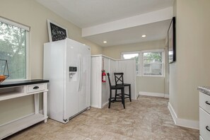 Compact kitchen with a refrigerator, countertop, and chair, featuring a window and a fire extinguisher.