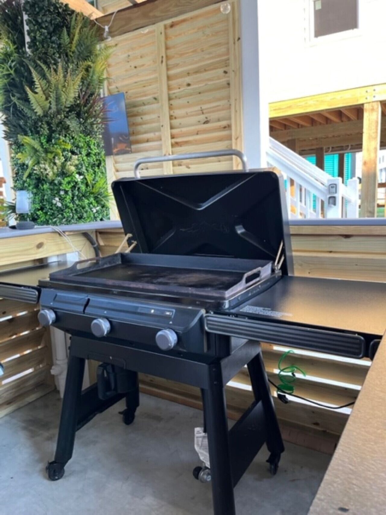 A portable grill with a control panel and a flat cooking surface, placed on a wooden deck.