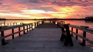 Un muelle de madera se extiende sobre el agua con un atardecer de fondo.