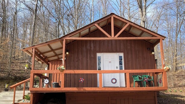 Eine Holzhütte mit Veranda, einer Tür und einem kleinen Garten mit Blumentöpfen.