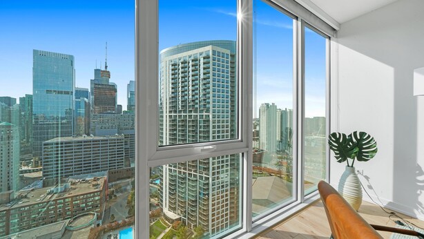 Una habitación moderna con grandes ventanales que ofrecen vista a la ciudad, piso de madera y una planta en el alféizar.