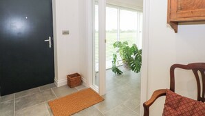 A hallway with a black door, a small wicker basket, a brown doormat, and a wooden chair with a patterned cushion. - Curlew (Malpas)