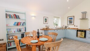 A modern kitchen with a wooden dining table, light blue cabinets, and a bookshelf filled with books. - Curlew (Malpas)