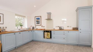 A kitchen with light blue cabinets, a wooden countertop, a built-in oven, and a window with a view of greenery. - Curlew (Malpas)