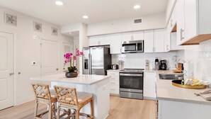Une cuisine moderne avec des meubles blancs, des appareils en acier inoxydable, un îlot central doté de tabourets et agrémentée d’orchidées décoratives.