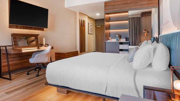 A modern hotel room with a large bed, a desk with a chair, a flat-screen TV, and a bathroom area.