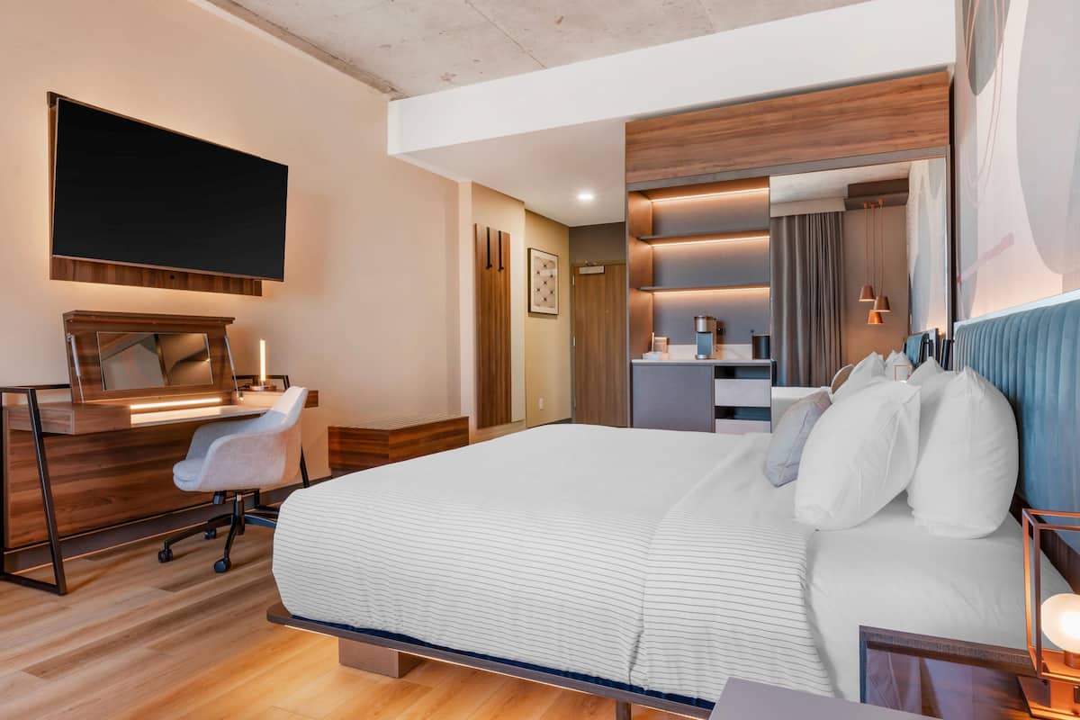 A modern hotel room with a large bed, a desk with a chair, a flat-screen TV, and a bathroom area.