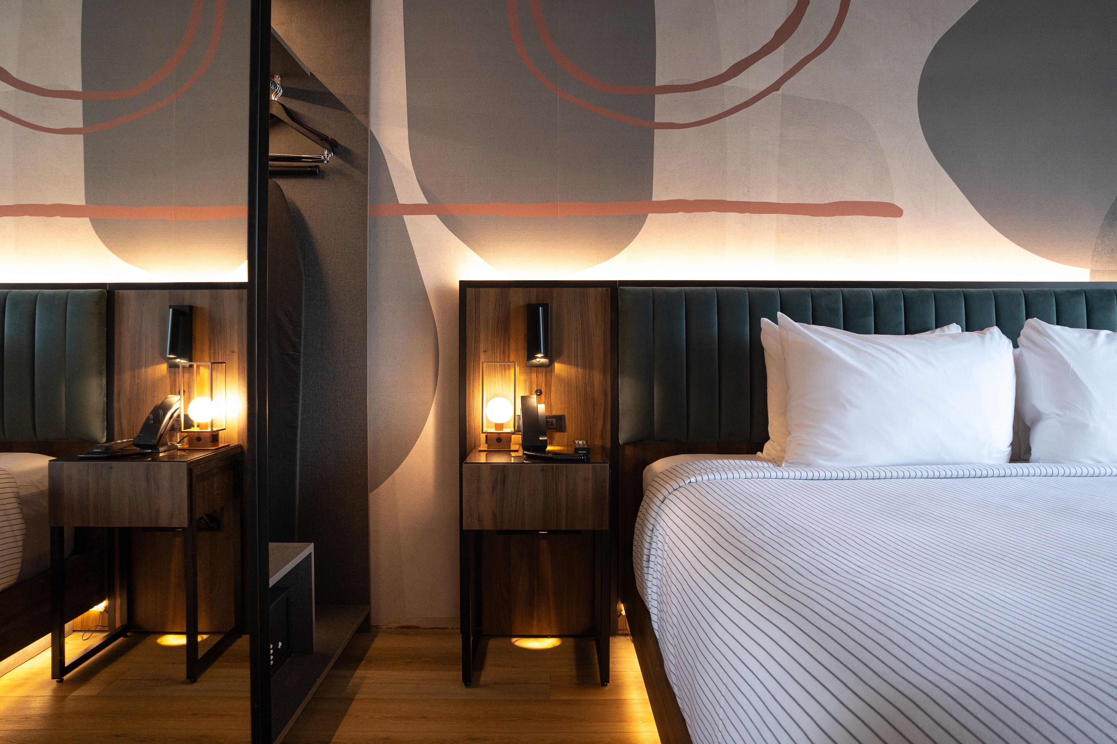 Ein Hotelzimmer mit einem großen Bett, Nachttischen, einem Schreibtisch und einer Wand mit abstrakten Gestaltungselementen.