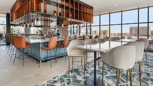 A modern bar area with a high ceiling, large windows, and a city view.
