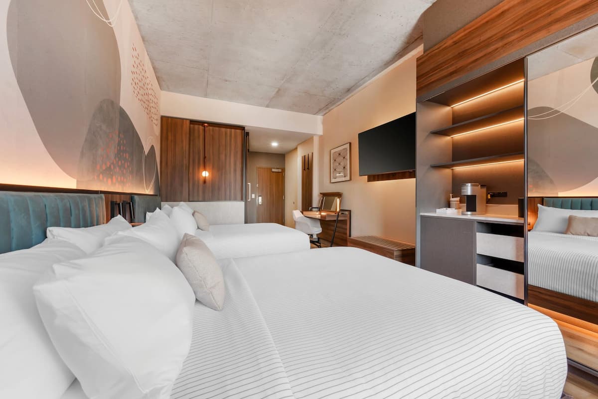 A hotel room with a large bed, a desk, a mirror, and a wardrobe.