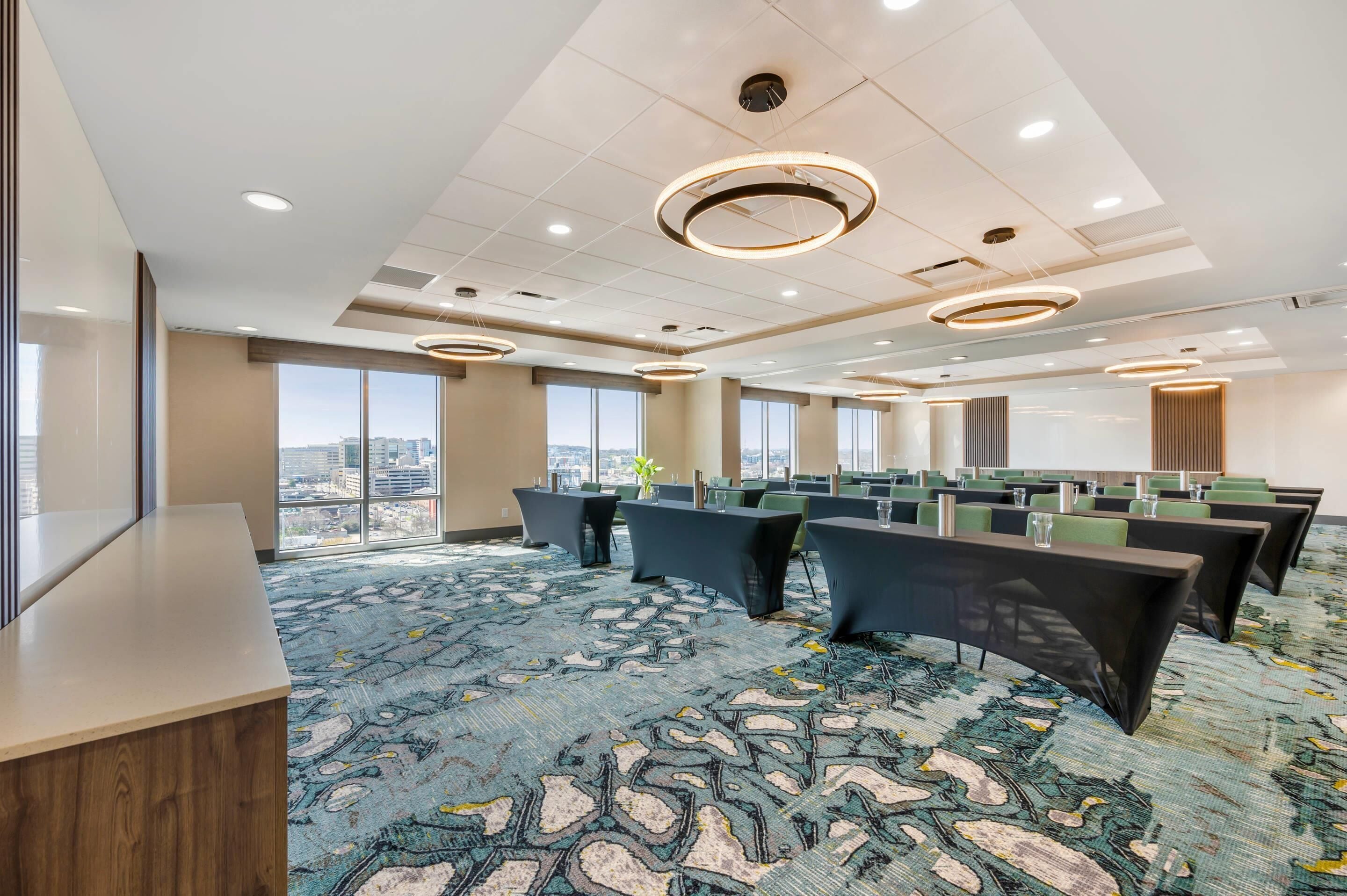 A conference room with multiple tables, large windows, and a patterned carpet.