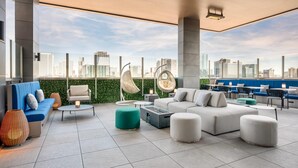 A rooftop lounge with a city view, including a sofa, chairs, ottomans, and a hanging chair.