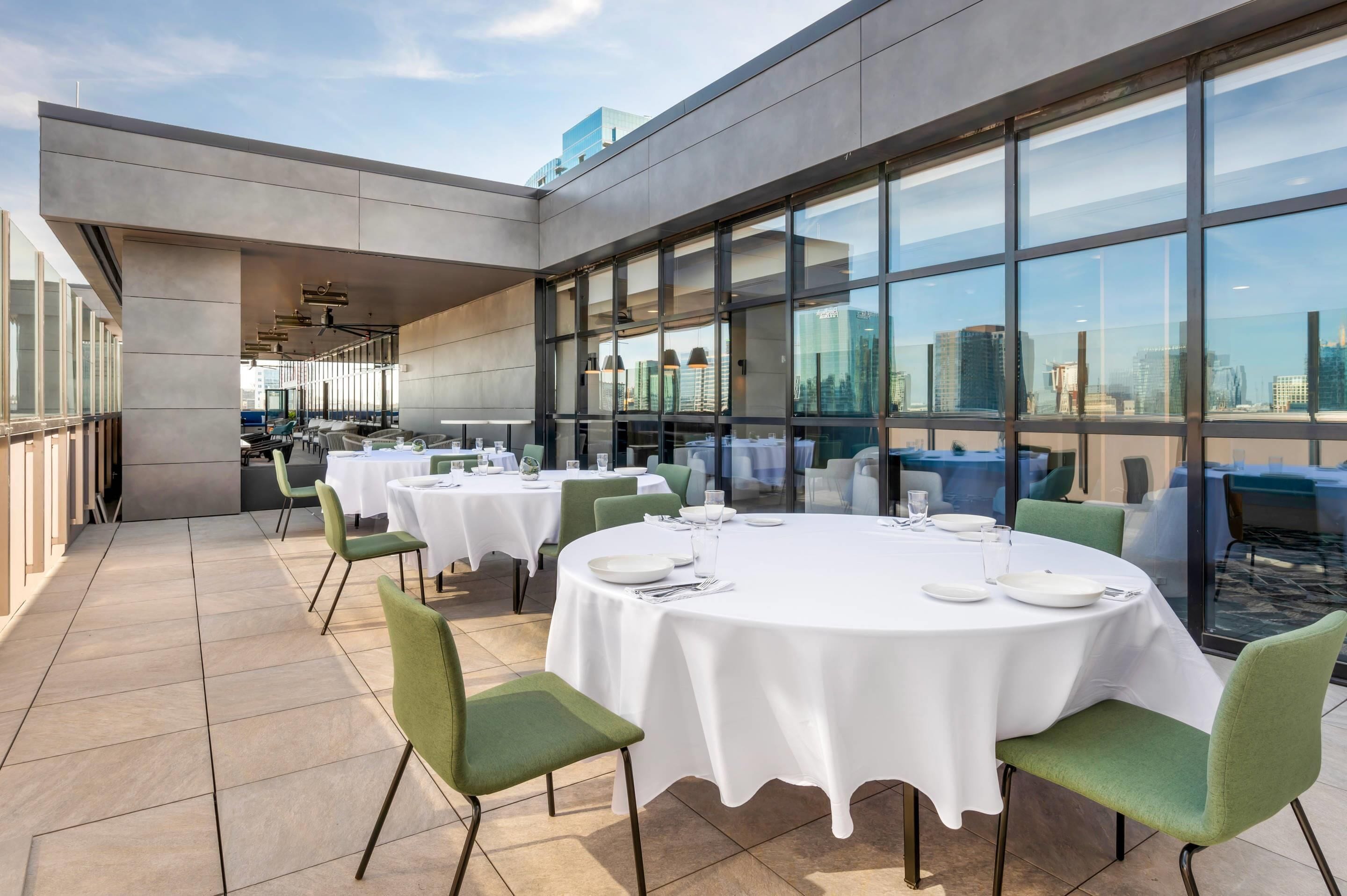 A rooftop dining area with round tables, chairs, and a city view.