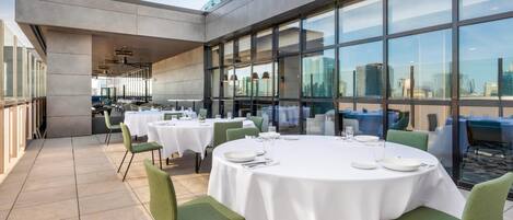 A rooftop dining area with round tables, chairs, and a city view.