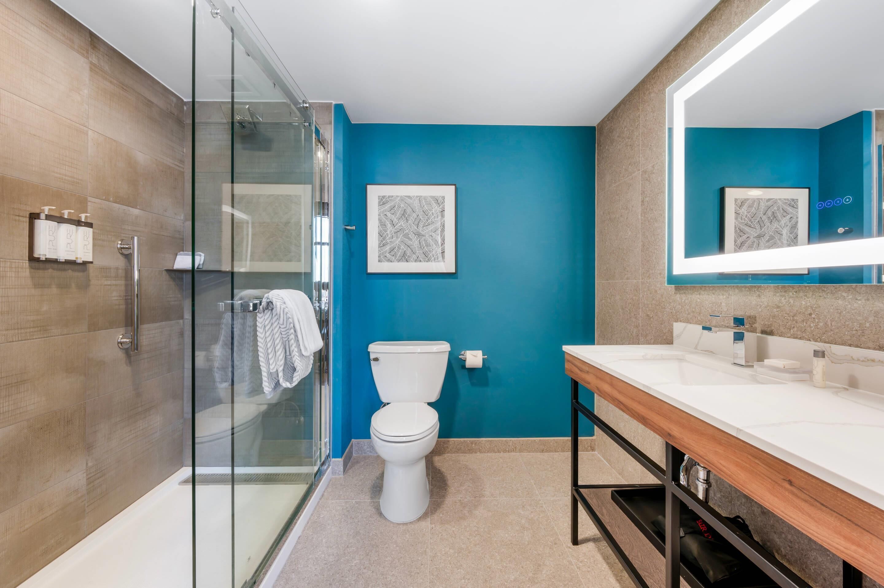 A modern bathroom with a glass shower enclosure, a white toilet, and a wooden vanity with a large mirror.