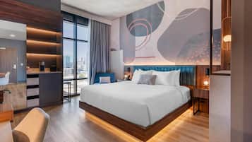 A modern hotel room with a large bed, a desk, and a view of the city.