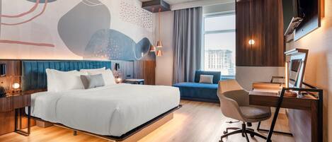 A modern hotel room with a large bed, a desk, a chair, and a view of the city.
