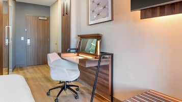 Una moderna camera d'albergo con una scrivania in legno, una sedia da ufficio bianca, un letto e un grande specchio.