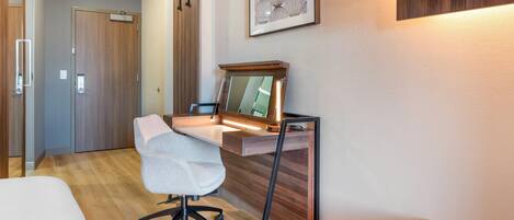 A modern hotel room with a wooden desk, a white office chair, a bed, and a large mirror.
