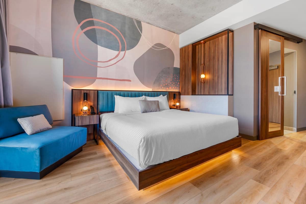 A modern bedroom with a large bed, a blue sofa, and a wooden wardrobe.