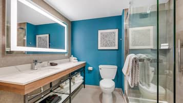 Ein Badezimmer mit blauer Wand, Toilette in Weiß, einer Duschkabine aus Glas und einem hölzernen Waschtisch mit Spiegel.