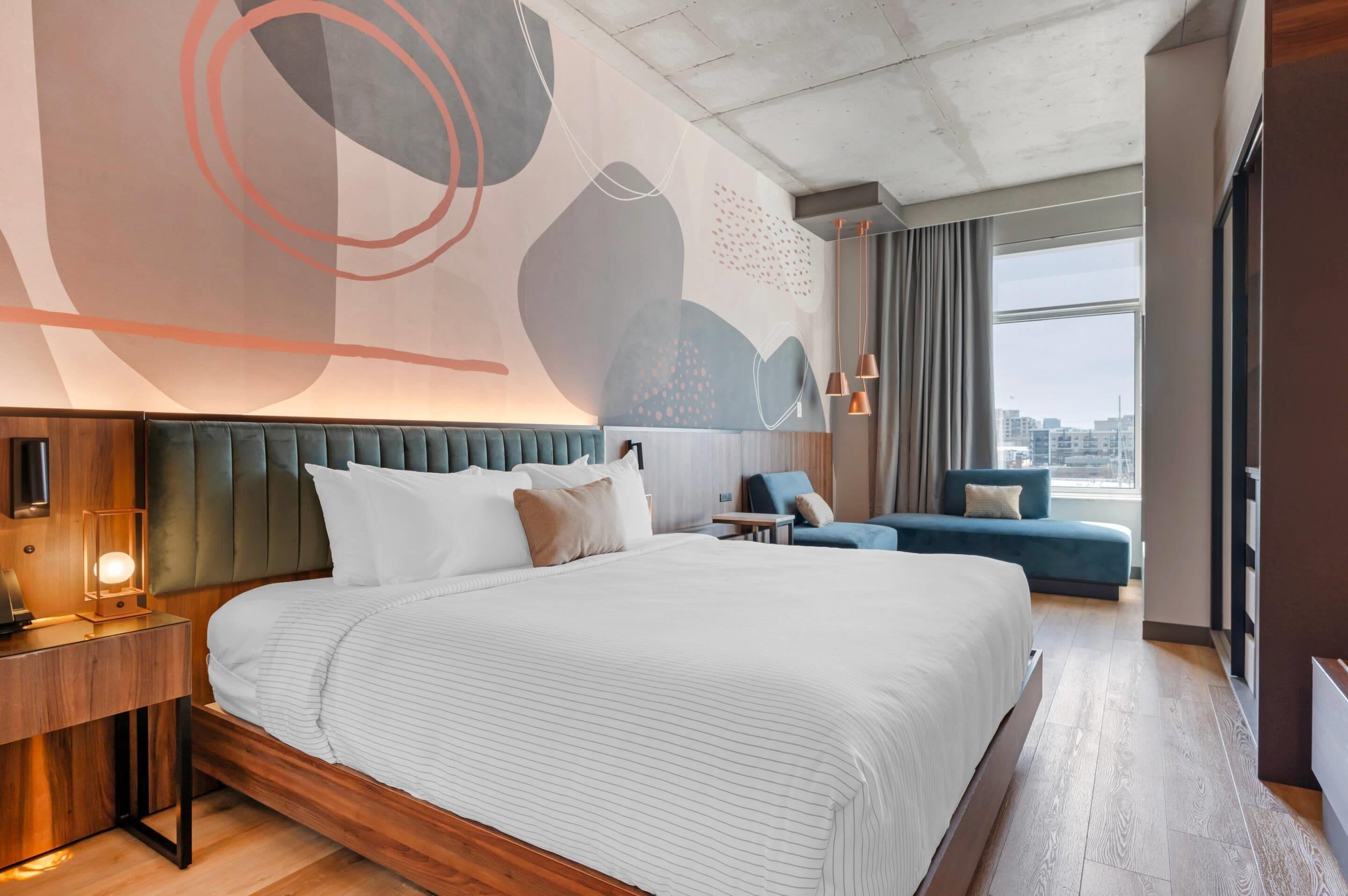 A modern hotel room with a large bed, a seating area, and a city view.