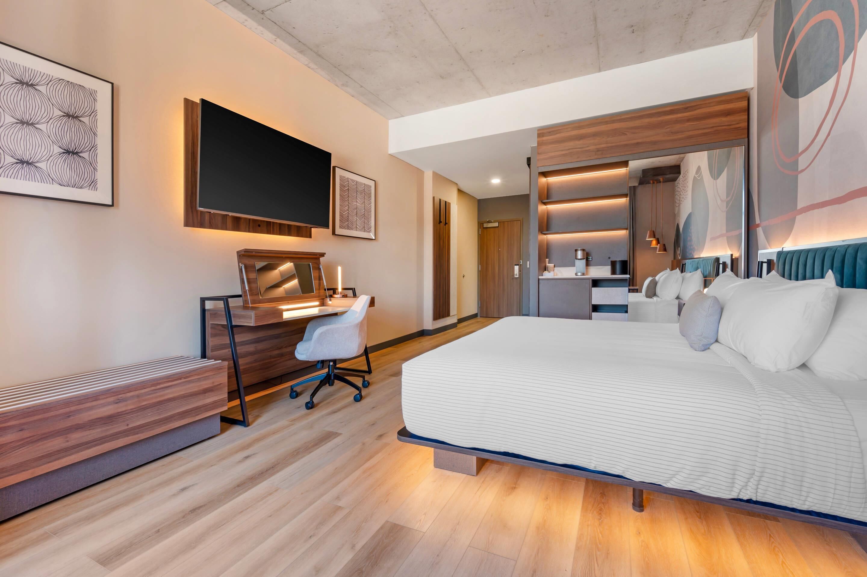 A modern hotel room with a large bed, a desk with a chair, a flat-screen TV, and a large artwork on the wall.