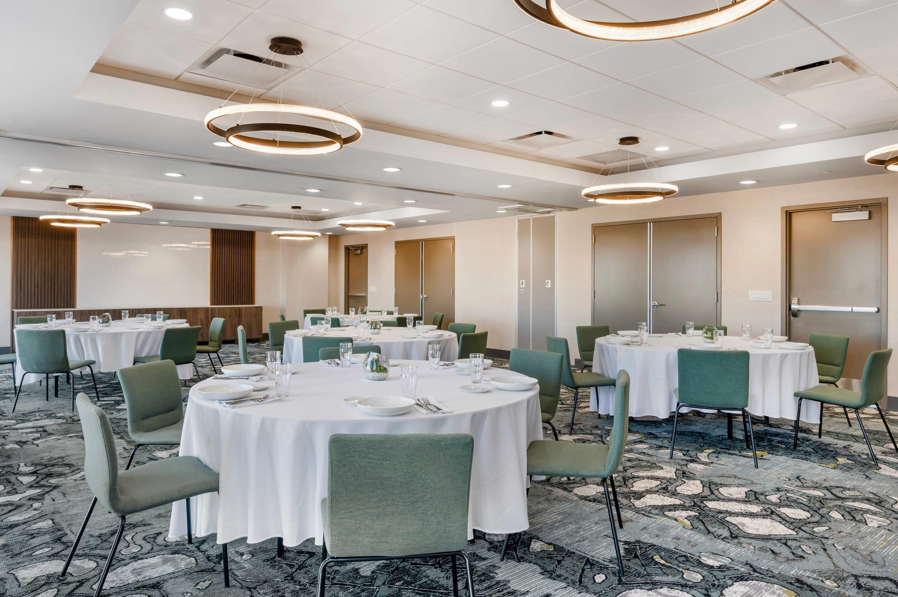 A conference room with round tables, green chairs, white tablecloths, and modern lighting fixtures.