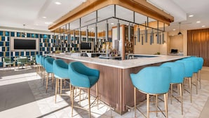A modern bar area with a curved counter, blue bar stools, and a mix of seating options including bar chairs and tables.
