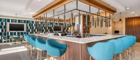 A modern bar area with a curved counter, blue bar stools, and a mix of seating options including bar chairs and tables.