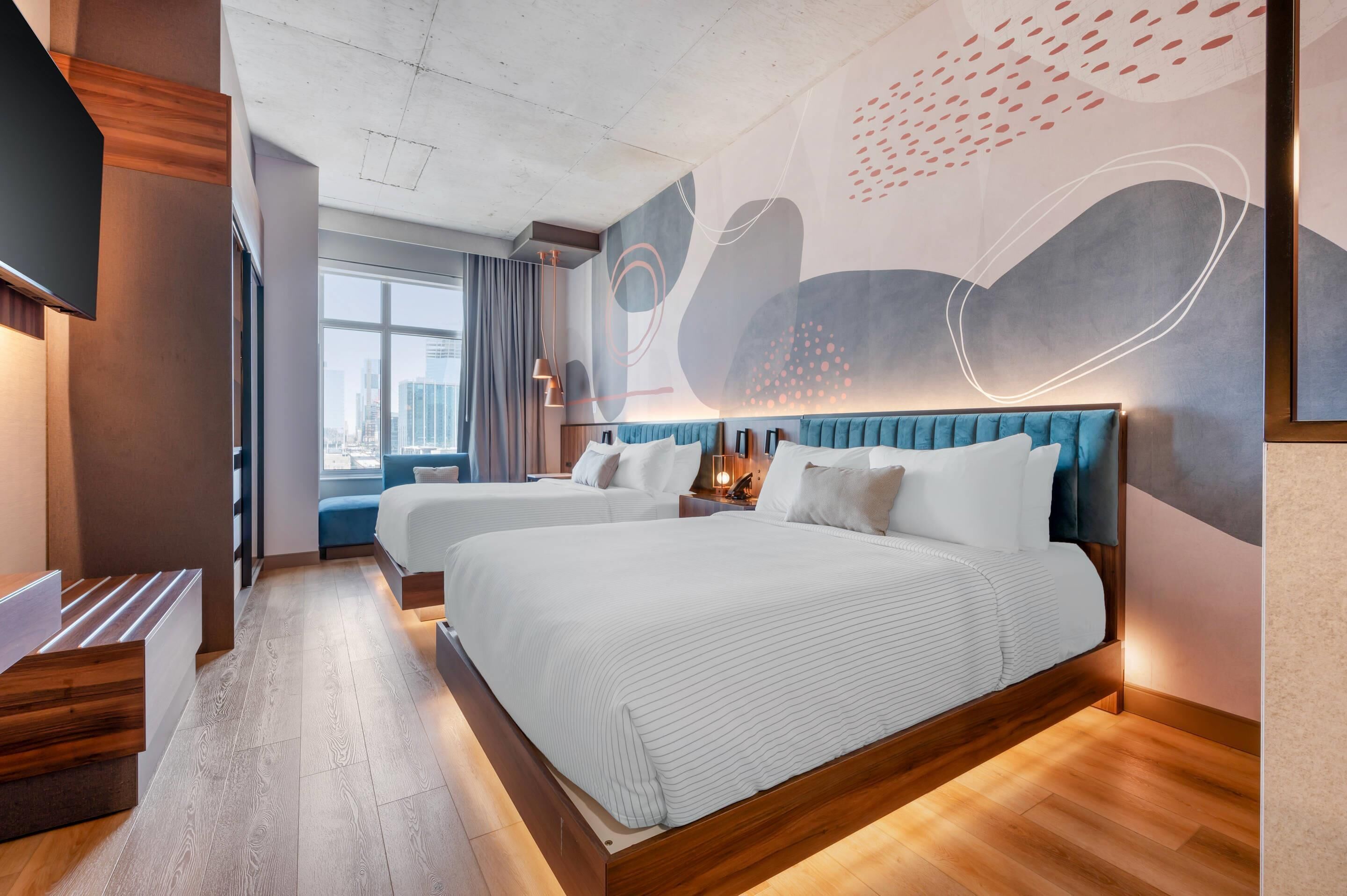 Una habitación de hotel moderna con dos camas, un ventanal grande y vistas a la ciudad.