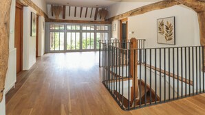 Ein geräumiger Raum mit Holzbalken, einer Treppe mit Metallgeländer und großen Fenstern, die natürliches Licht hereinlassen.
