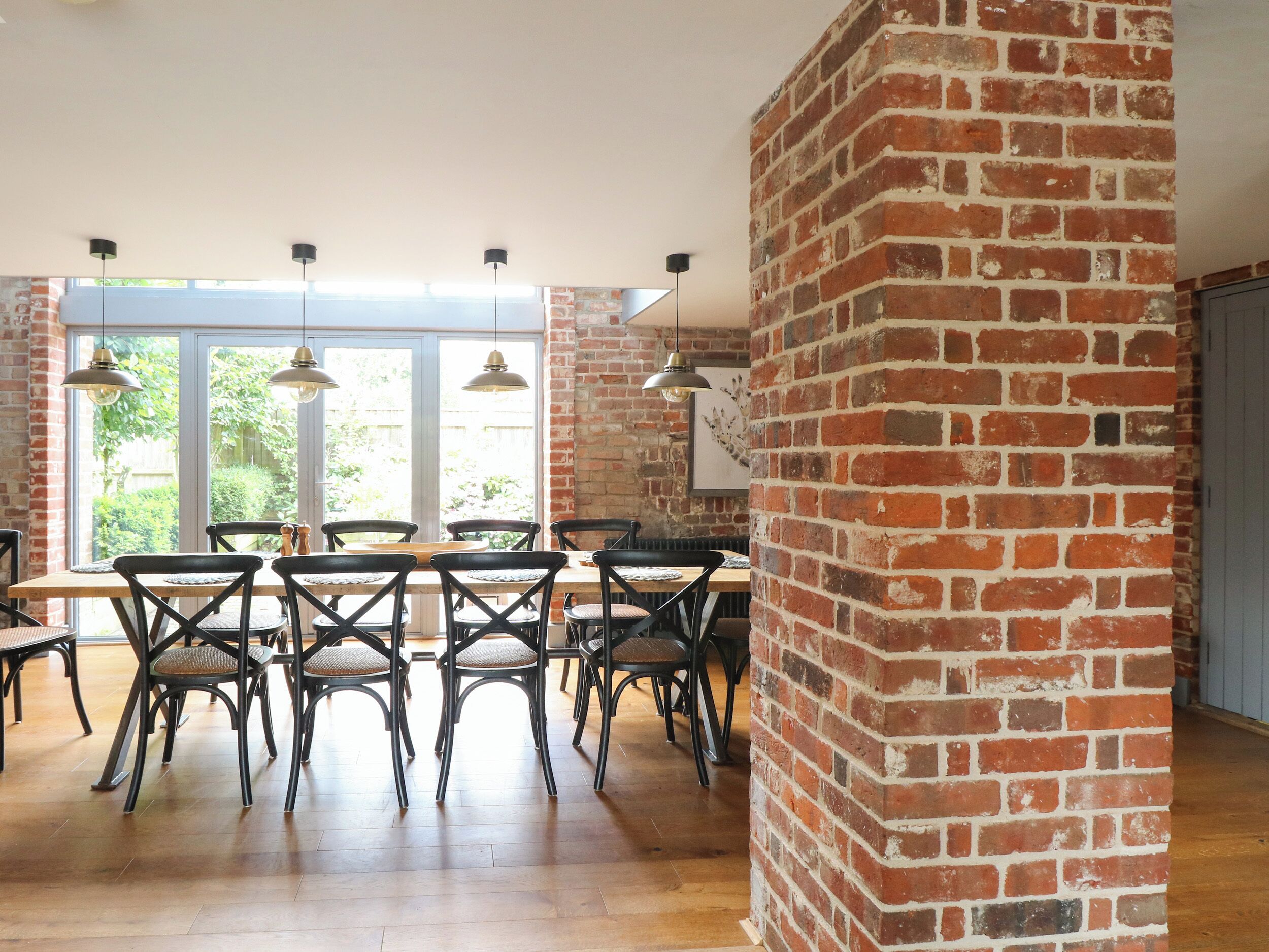 A dining area with a brick wall, wooden table, and black chairs.