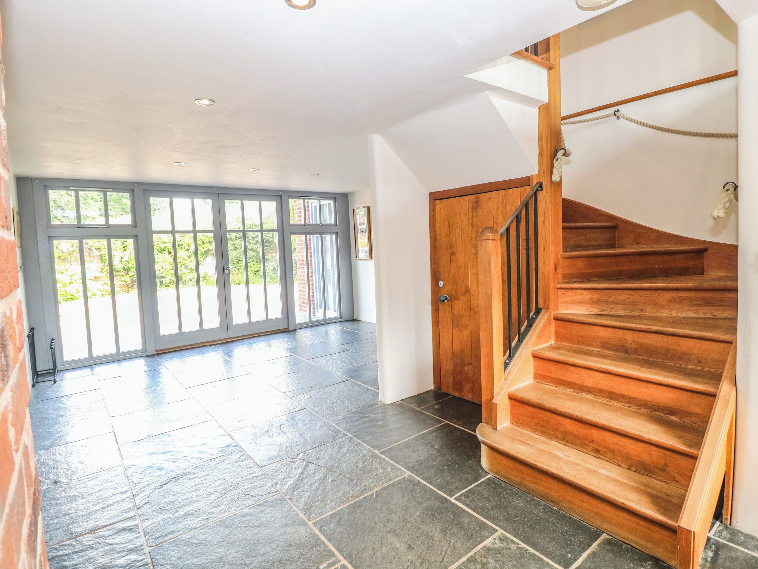 A spacious room with a wooden staircase and a large sliding glass door leading to a garden.