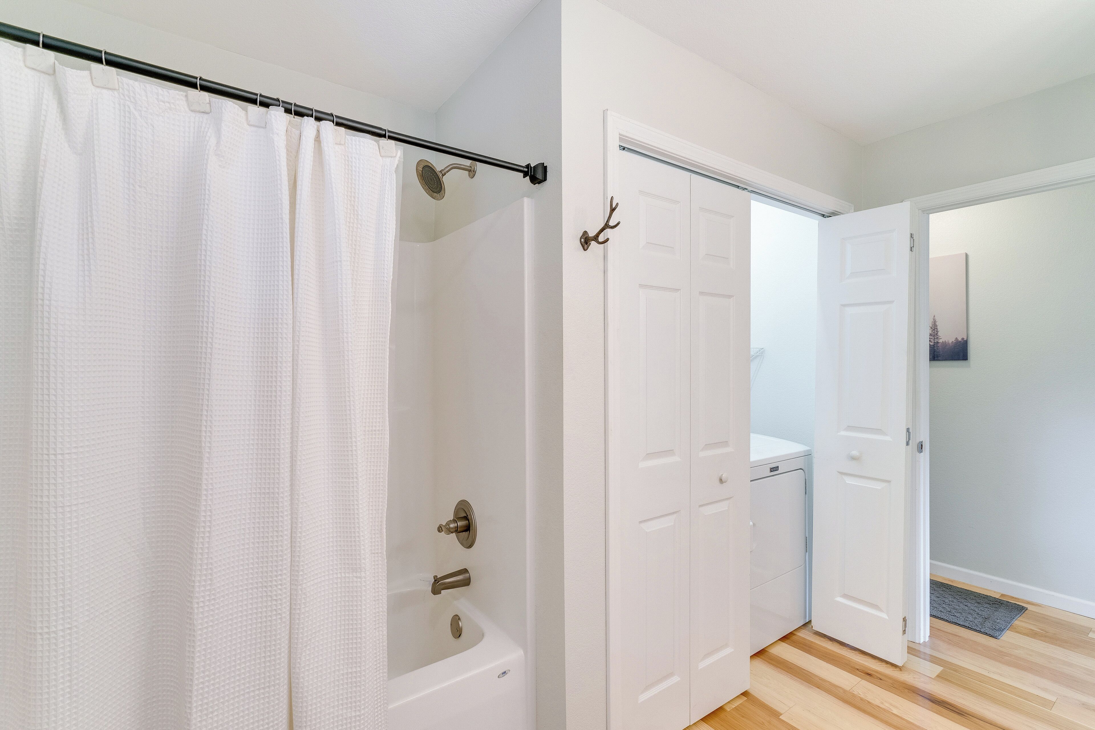 A bathroom with a bathtub, a shower curtain, and a door with a coat hook.