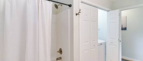 A bathroom with a bathtub, a shower curtain, and a door with a coat hook.