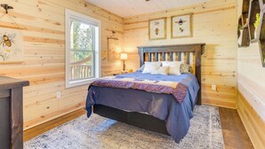 Ein Schlafzimmer einer Holzhütte mit Bett, Deckenventilator, Fenster und Wandbild.
