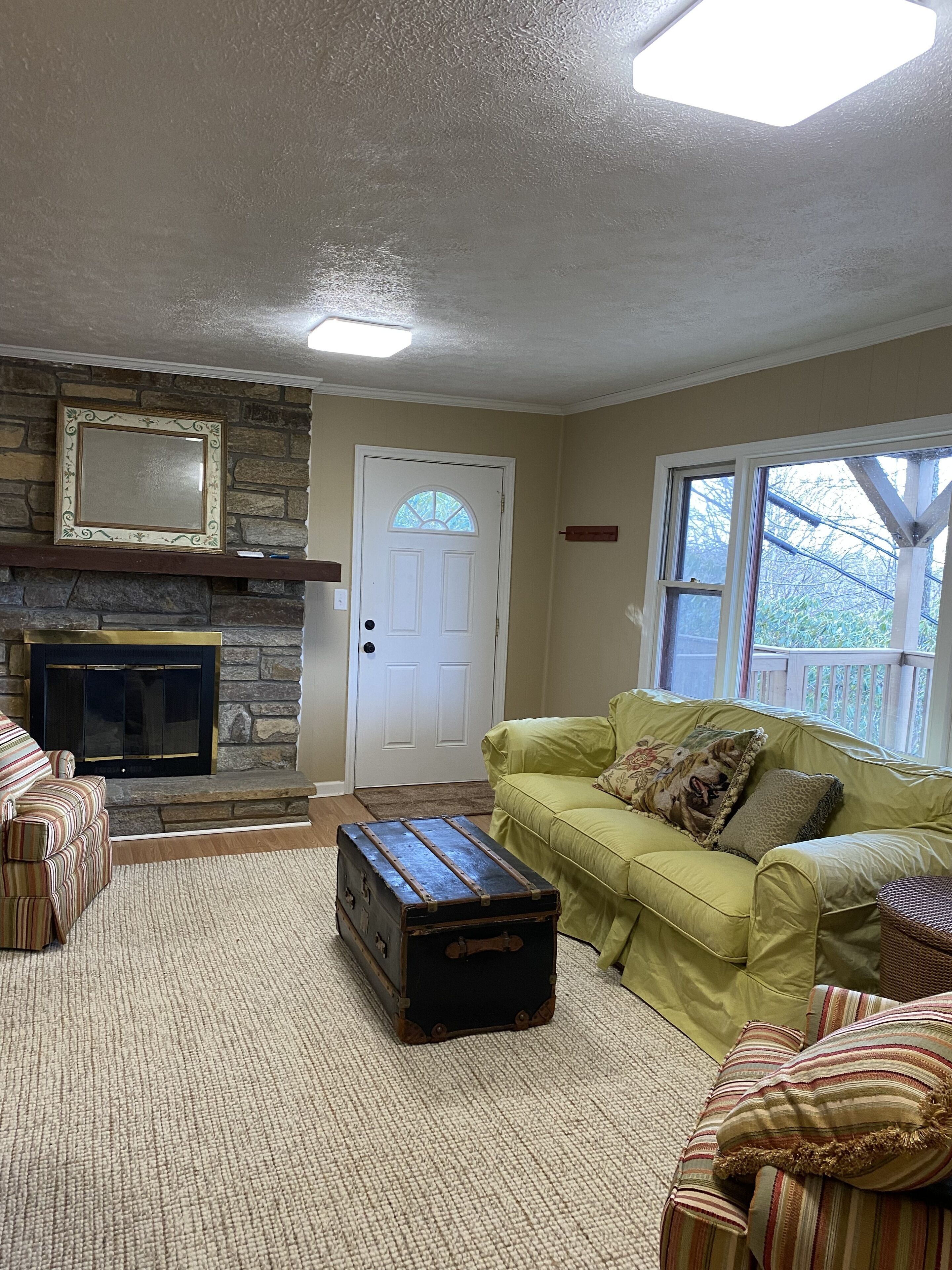 A living room with a stone fireplace, a green sofa, a striped armchair, and a vintage trunk.
