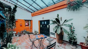 A covered patio with a tiled floor, a table with chairs, and various potted plants.