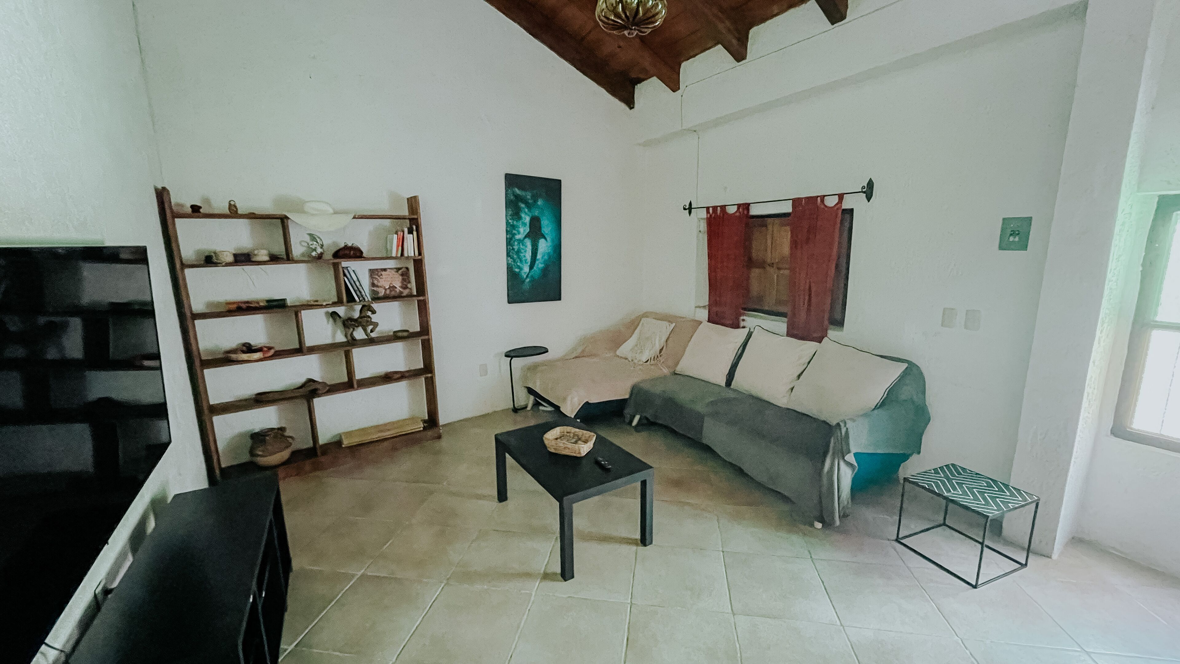 Un salon comprenant un canapé, une table basse, une bibliothèque et une fenêtre avec des rideaux.