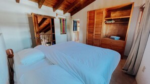 A bedroom with a bed, wooden wardrobe, and a small shelf.