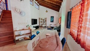 A spacious living room with a high ceiling, a dining area with a table and chairs, and a staircase leading to another level.