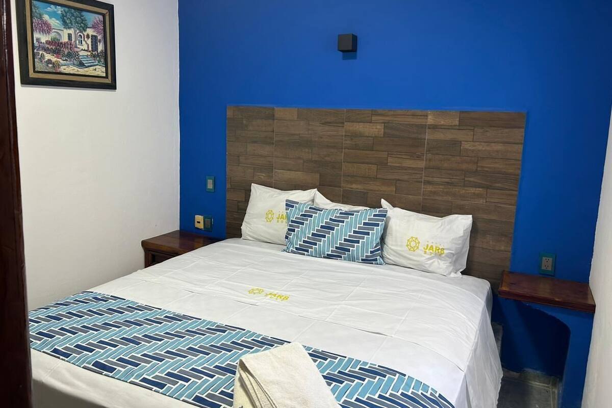 A bedroom with a blue accent wall, a wooden headboard, and a bed with patterned bedding.