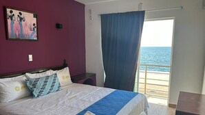 A hotel room with a bed, a painting on the wall, a view of the sea through a window, and a curtain. - Hotel Jar8 Bule (Boca del Río)