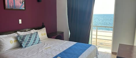 Una habitación de hotel con cama, un cuadro en la pared, vista al mar por la ventana y una cortina.