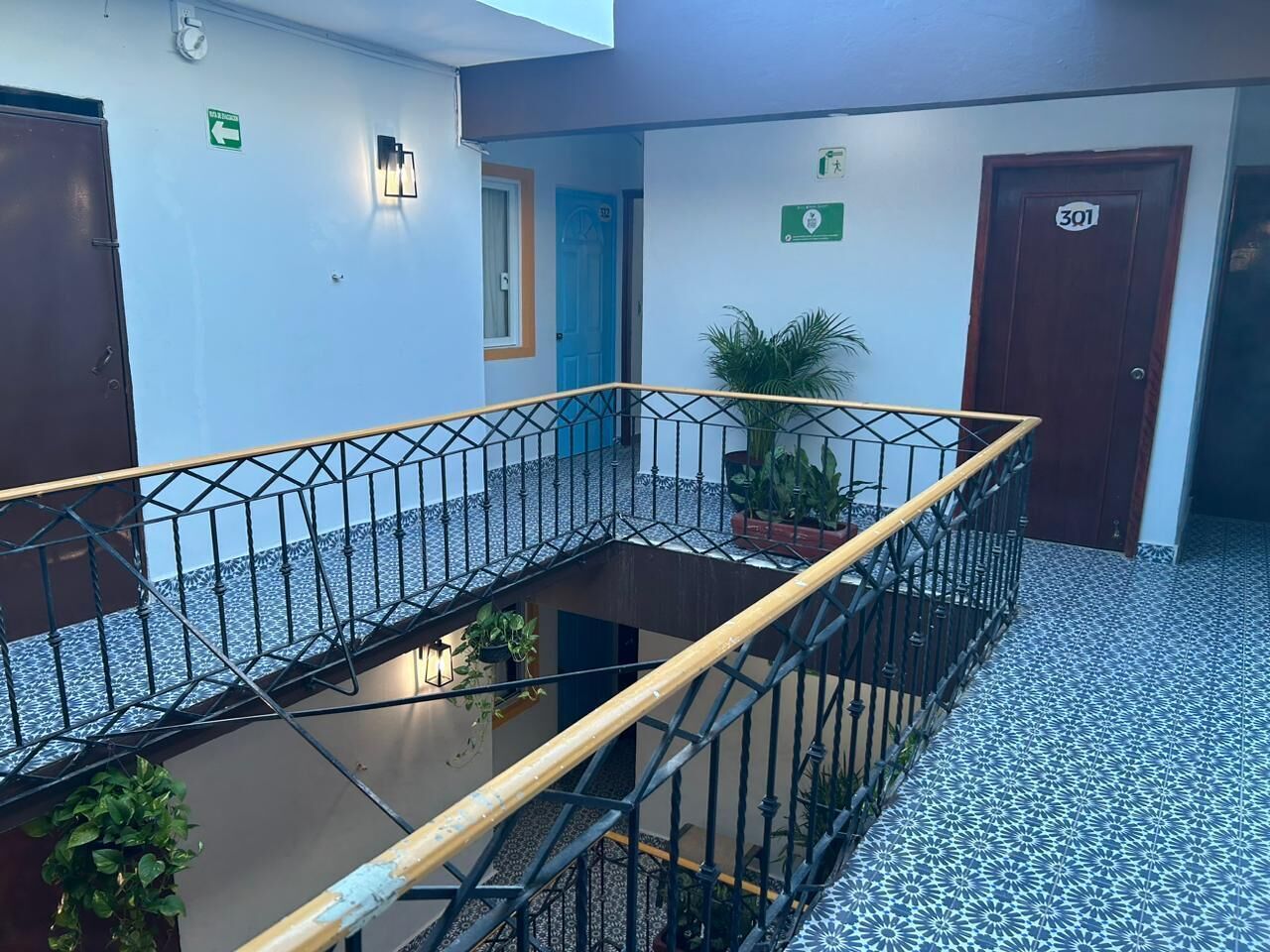 A multi-level indoor space with a central open area, metal railings, and potted plants.