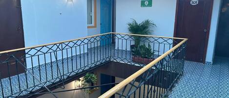 A multi-level indoor space with a central open area, metal railings, and potted plants.