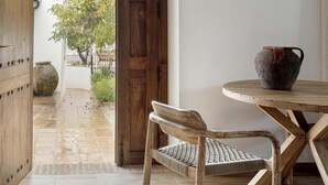 A wooden door leading to a tiled patio with a woven chair and a rustic table with a vase.